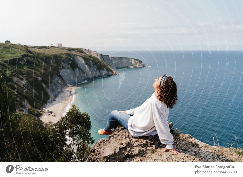 relaxed woman sitting on top of the cliff looking at sea landscape in Asturias. Relax and nature concept caucasian relaxing cliffs daytime 30s balance serene