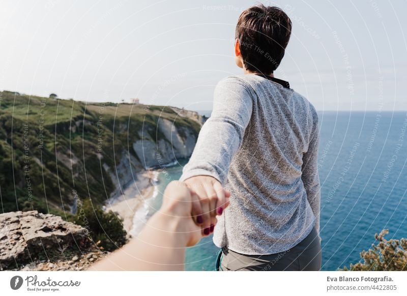 back view of Girlfriend holding hand of boyfriend during hiking on top on the cliff. Sea view. Relax and nature concept woman relax enjoying young together