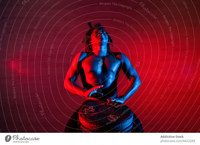 African American man playing Djembe drum in studio djembe percussion music musician neon light male black ethnic african american blue red color glow illuminate