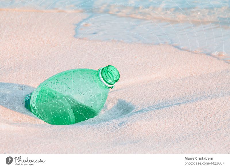 Close up of a green plastic water bottle buried in the sandy beach plastic pollution ocean pollution single use plastic environmental activism social issues