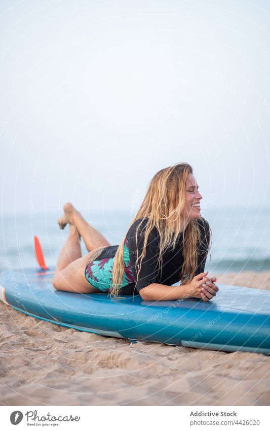 Cheerful woman lying on SUP board on beach surfer paddleboard sup board swimsuit smile seashore summer female vacation swimwear recreation enjoy positive