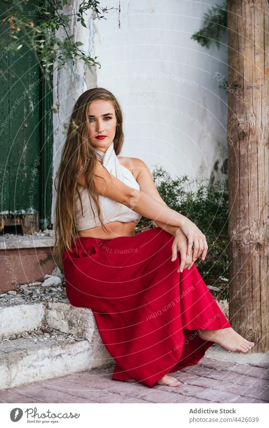 Graceful woman sitting in patio grace red skirt bright color garden charming summer female plant style house green stone step barefoot long hair carefree fresh