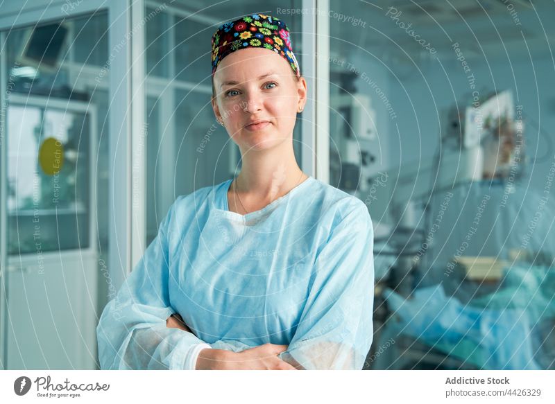 Confident surgeon with crossed arms in clinic self assured arms crossed smile professional uniform woman glass wall portrait specialist sterile doctor surgical