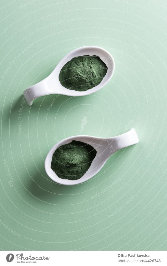 Two spoon bowls with chlorella or spirulina powder spoons paper background green background light two porcelain shape above vertical white seaweed chlorophyll