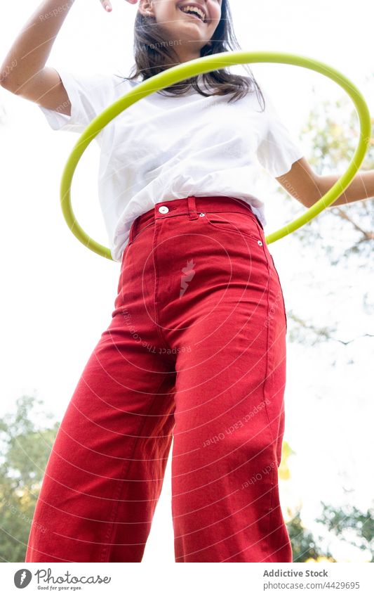 Crop smiling active teenager twisting hoop in park hula smile recreation leisure free time glad enjoy spare time activity red jeans content colorful wellness