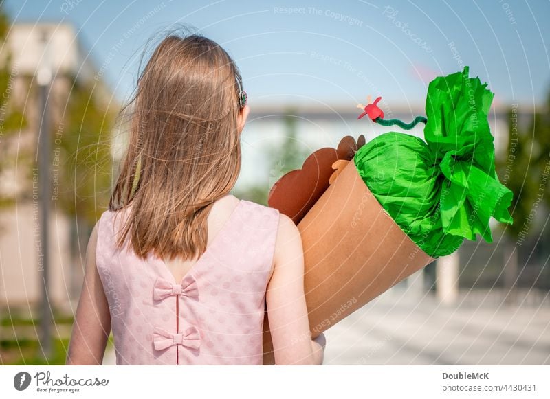 A girl stands in front of the school with a school bag on her arm Girl School candy cone sugar cone First day at school Child Colour photo Infancy Education