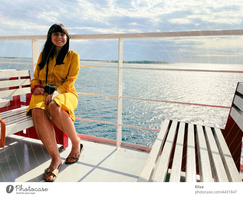 A woman in a yellow dress sits on a bench on a ferry in the sunshine Ferry Woman ship Ocean Vacation & Travel Summer Dress Smiling Railing Passenger ship Sit