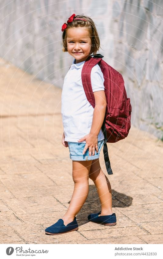 Schoolgirl in casual clothes with rucksack on urban walkway schoolgirl curious childhood back to school pavement stone wall charming dreamy tiled ribbed gentle