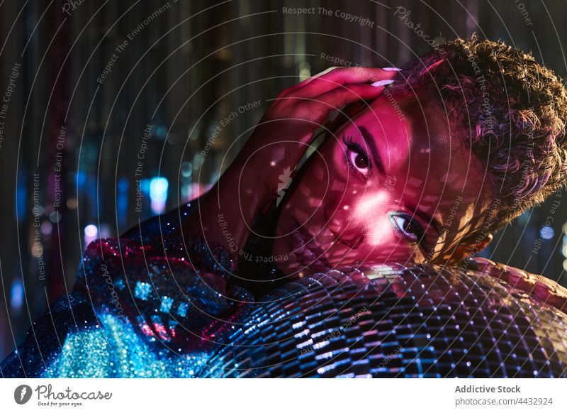 Stylish black model with makeup leaning on disco ball touch face individuality stylish gaze woman nightclub portrait tilt style cool haircut african american