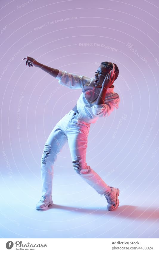 Active black dancer in headset dancing hip hop on light background choreography energy motion fashion woman using gadget active device mouth opened fast perform
