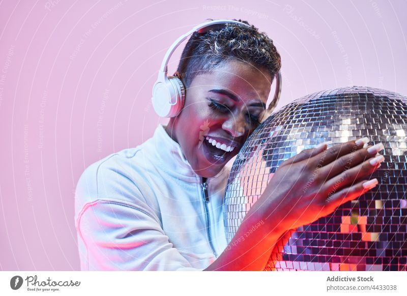 Trendy smiling black model in headphones with disco ball cheerful fashion style wireless woman happy portrait using device gadget light glitter ball mirror ball