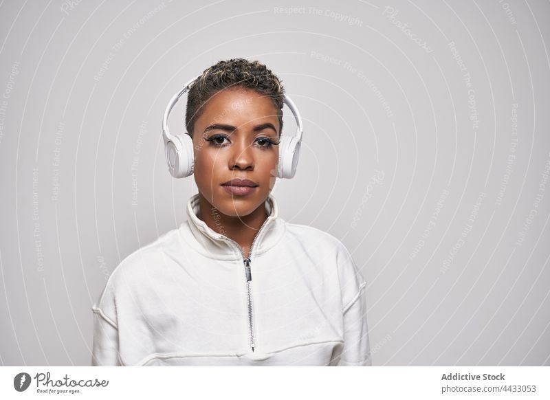 Black woman listening to music in headset standing on gray background choreography energy fashion using gadget active device headphones dancer hip hop style