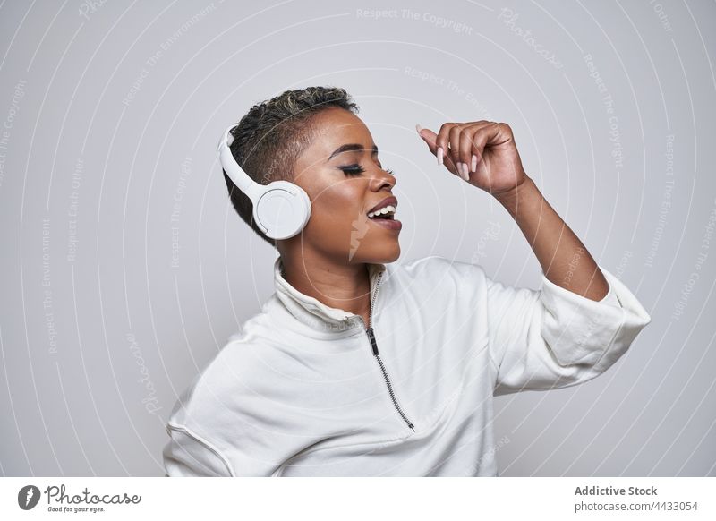 Active black dancer in headset dancing hip hop on gray background choreography energy motion fashion woman using gadget active device mouth opened fast perform