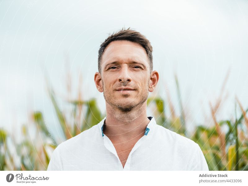 Unshaven man in countryside field in daytime sincere friendly kind calm gaze sky portrait casual wear white color natural serene confident unshaven modern
