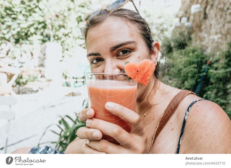 Woman smiling to camera while holding a fresh summer drink on a garden and covering his face with the drink, summer holidays concept portrait businesswoman