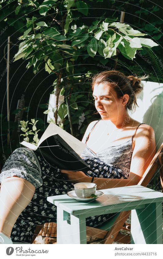 Woman reading a book while reclined on a chair during a sunny day, copy space, relax and hobby concepts, social network education comfortable furniture joy