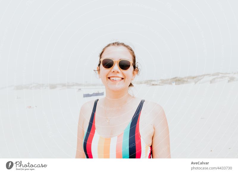 Young woman in a swimsuit and sunglasses smiles to camera during a sunny day at the beach, liberty and holiday concept,portrait fun swimwear emotion one person