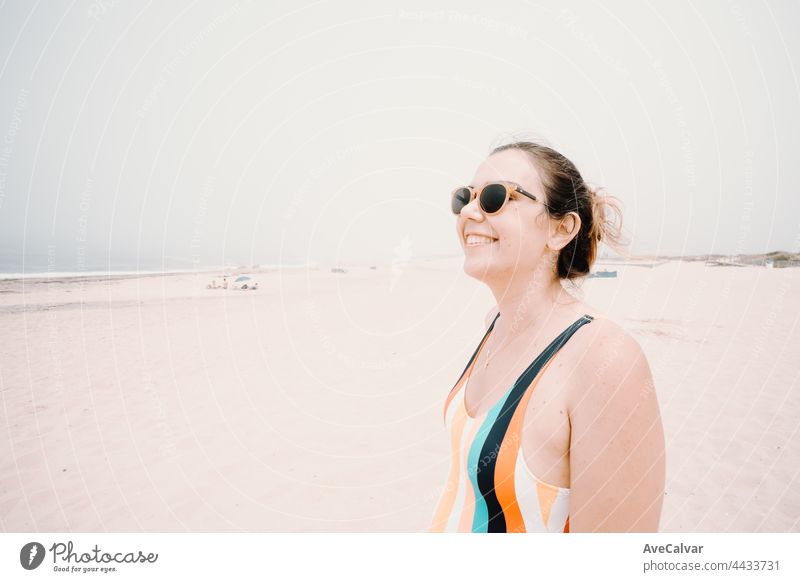 Young woman in a swimsuit and sunglasses smiles during a sunny day at the beach, liberty and holiday concept, copy space fun swimwear emotion one person
