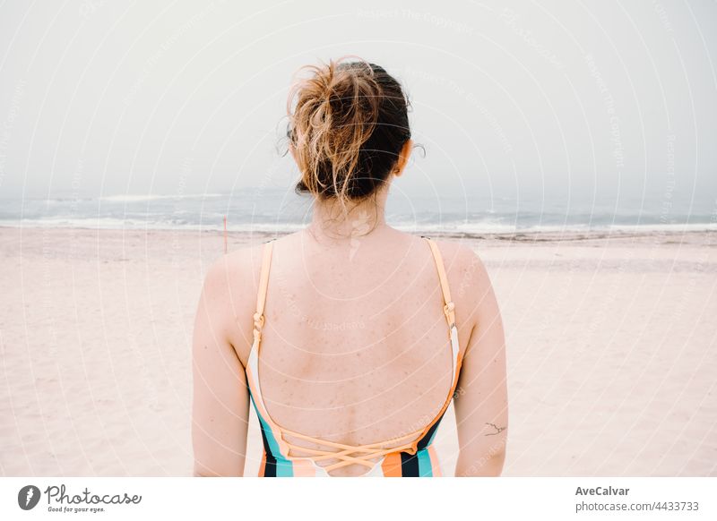 Back of a young woman in a swim suit, melancholic beach, holiday, after summer feeling fun swimwear emotion one person carefree sunbathing young adult headshot