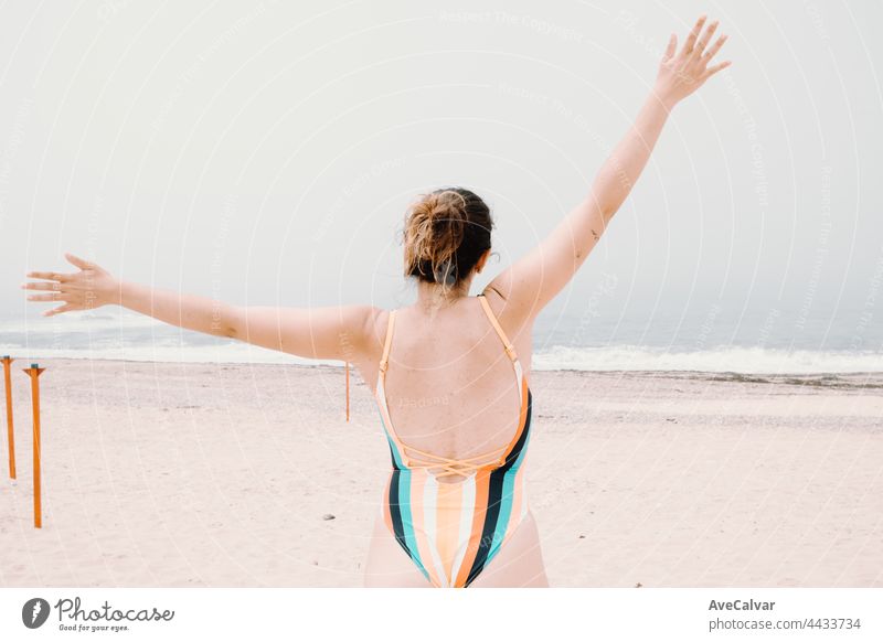 Young woman in a swimsuit back, jumping and celebrating during a sunny day at the beach, liberty and holiday concept, copy space fun swimwear emotion one person