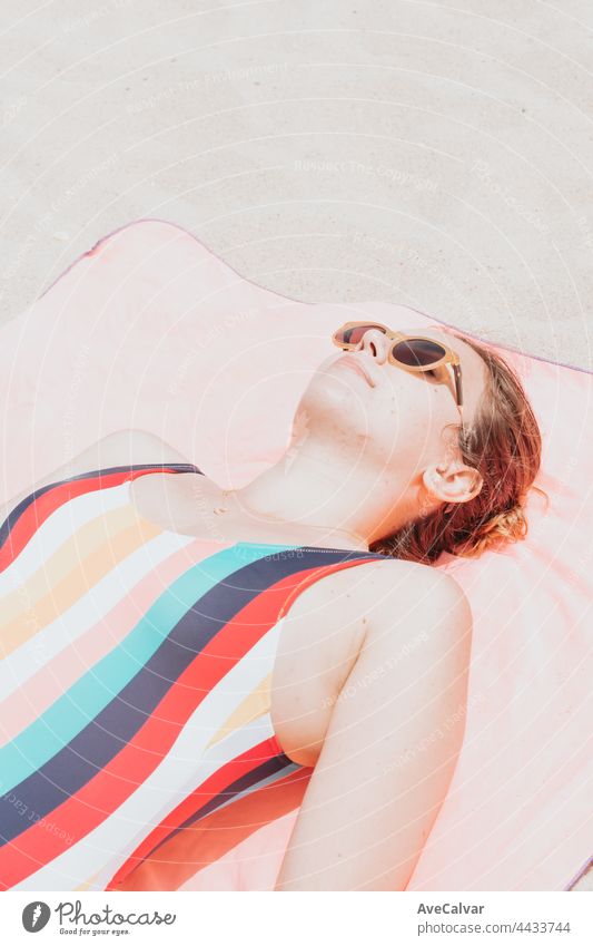 Image from above of a young woman in a colorful swimsuit taking a sunbath while using the sunglasses, holiday and rest concept. social media marketing, modern low cost traveling