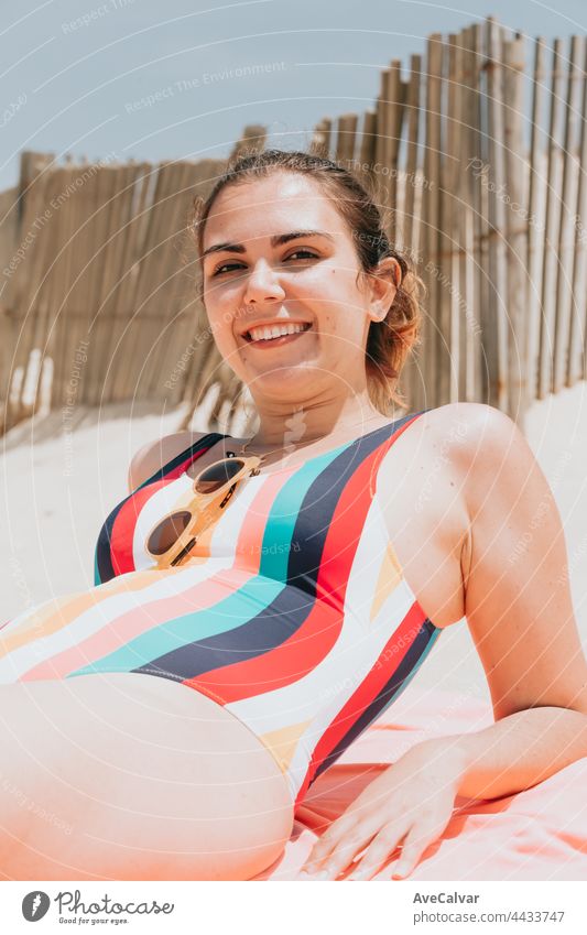Young woman smiles to camera while wearing a colorful swimsuit at the beach, travel young holiday concept, copy space, social network, sunglasses user concept