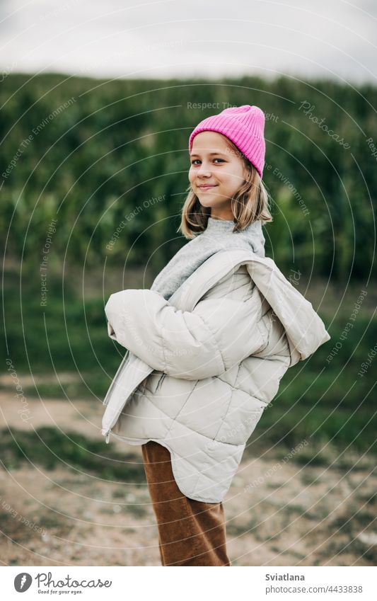 A teenage girl in a stylish image and a pink cap stands against the background of a corn field autumn yellow cornfield teenager cloak laugh lifestyle play cute