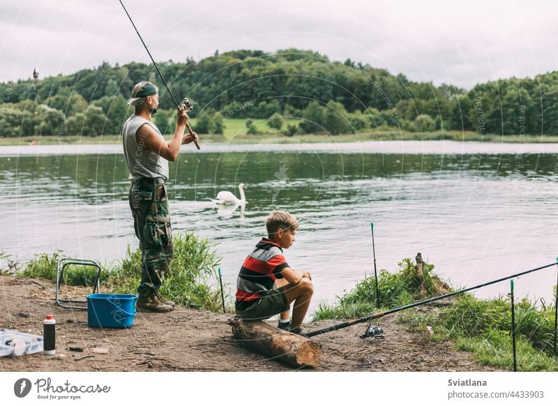 A young man teaches his children to fish during a family vacation at a camping site. Hobbies, vacations, weekends, fishing together boy lake shore teaching dad