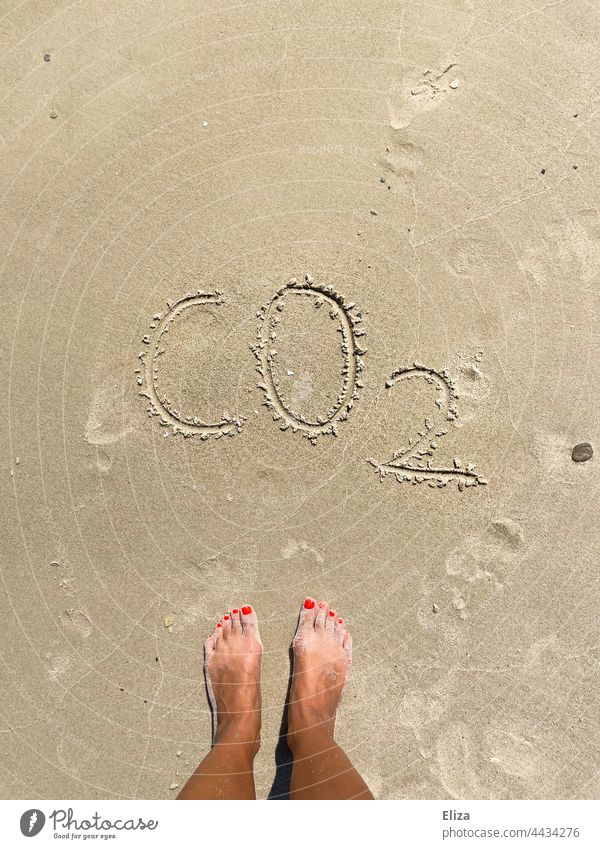 Feet in the sand in front of the word CO2 - Climate crisis and travel concept Sand co2 climate crisis Carbon dioxide CO2 emission vacation Beach Ocean co2 load