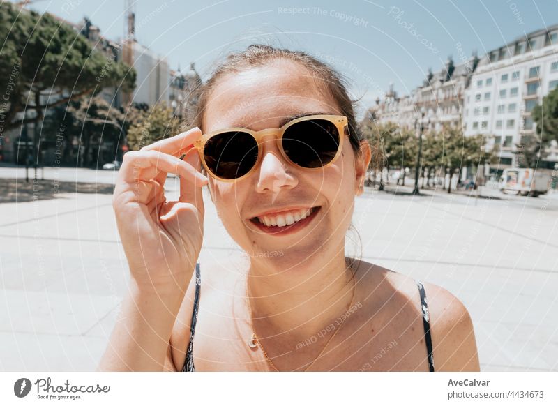 Young woman using sunglasses smiling a lot while touching them, sunglasses concept, summer and travel,copy space dress relaxation carefree fashionable joy hair