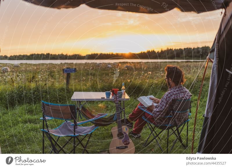 Man reading a book at a campsite. View from a tent camping meadow grass field rural green countryside adventure hiking Wilderness wild vacation travel active