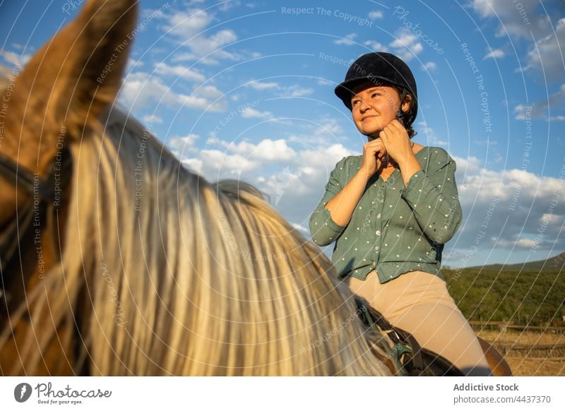 Contemplative woman on horse under cloudy sky in countryside horseback mare dreamy helmet protect equine animal stallion ride riding school livestock idyllic