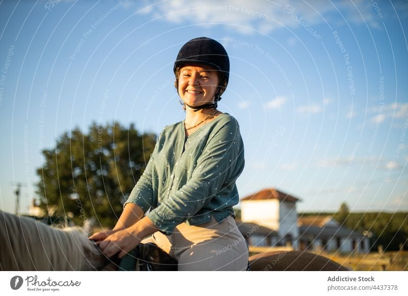 Contemplative woman on horse under cloudy sky in countryside horseback mare cheerful dreamy helmet protect equine animal happy stallion ride riding school