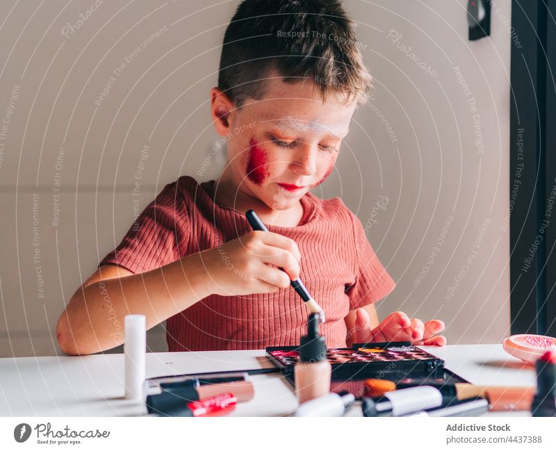 Boy applying eyeshadow on face in house room boy makeup applicator beauty cosmetic decorative messy having fun portrait childhood palette product assorted table