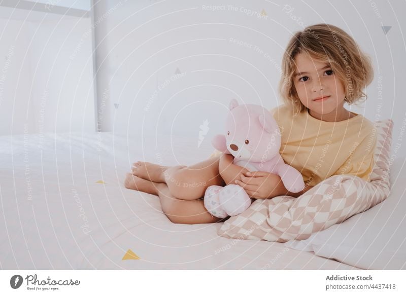 Girl with toy bear resting on bed in house girl embrace charming childhood kind portrait soft plush gentle barefoot home blanket ornament domestic gaze bedroom