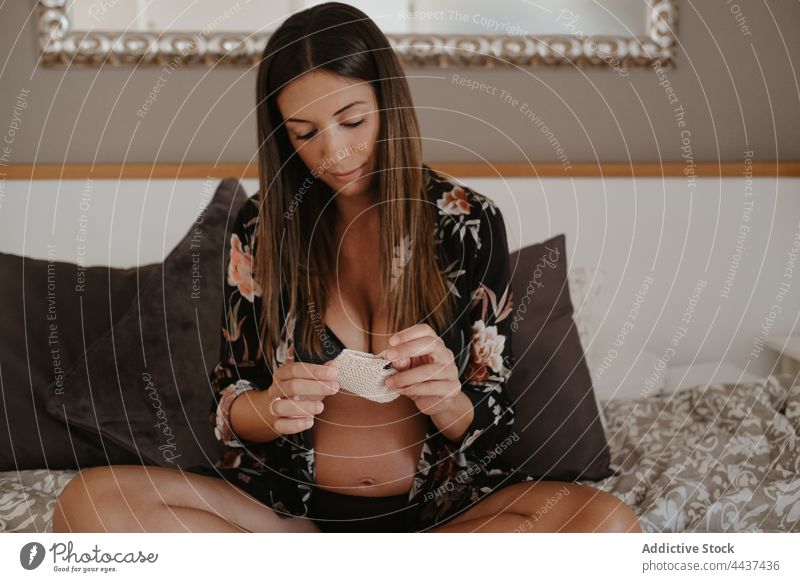 Pregnant woman in lingerie resting on bed at home pregnant anticipate sock maternal expect calm legs crossed small pregnancy await belly floral ornament cushion