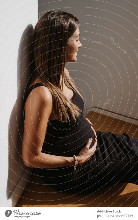 Smiling pregnant woman touching belly on floor at home touch belly pregnancy dreamy eyes closed maternal await anticipate idyllic house expect smile mindfulness