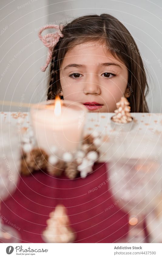 Gentle girl admiring burning candle on Christmas Day contemplate wish christmas new year celebrate magic festive home flame child xmas occasion focus glass