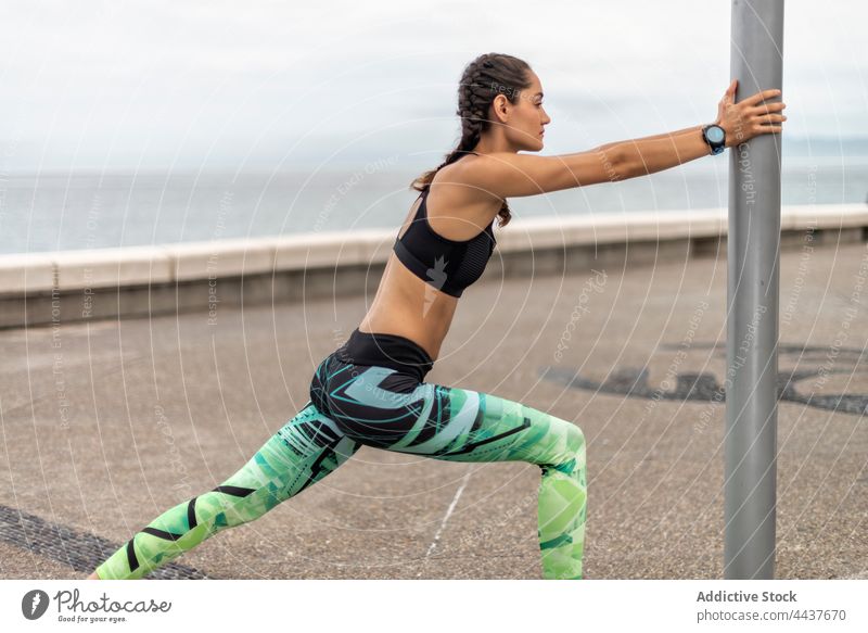 Slender sportswoman warming up during training on promenade runner stretch warm up workout embankment slim fit athlete female lean pillar flexible wellbeing