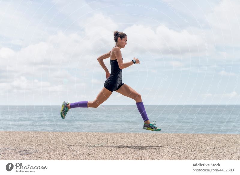Active sportswoman running along embankment runner jump moment cardio training summer athlete female workout above ground energy fit dynamic sportswear slim