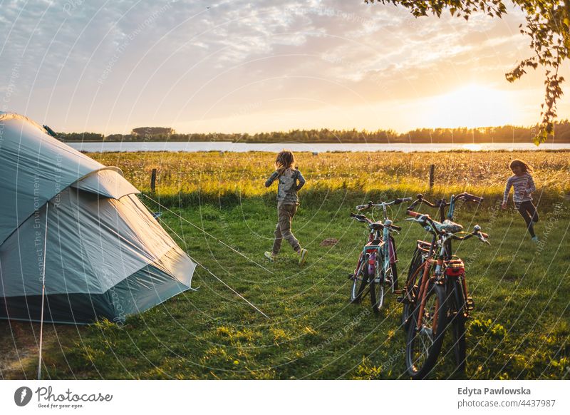 Children playing on the campsite running playful fun joy children family kids camping tent bike cycling meadow grass field rural green countryside adventure