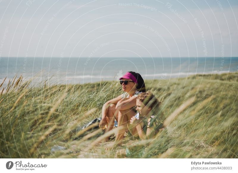 Mother and daughter sitting in the grass by the sea wilderness field mum mother person beautiful active adventure beach blue child childhood children cute day