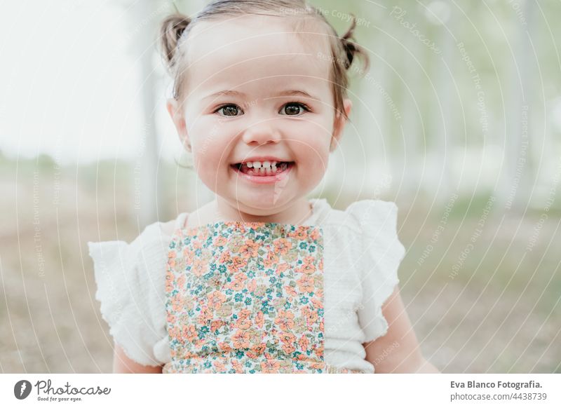 close up portrait of happy baby girl having fun outdoors in trees path. Children, fun and nature concept forest childhood smiling run caucasian Spain dress