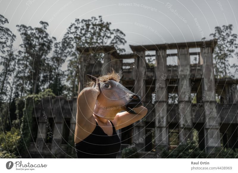 Female in horse mask with hands in head in front of horror abandoned house. woman afraid halloween old mansion fear mysterious terror background person scary