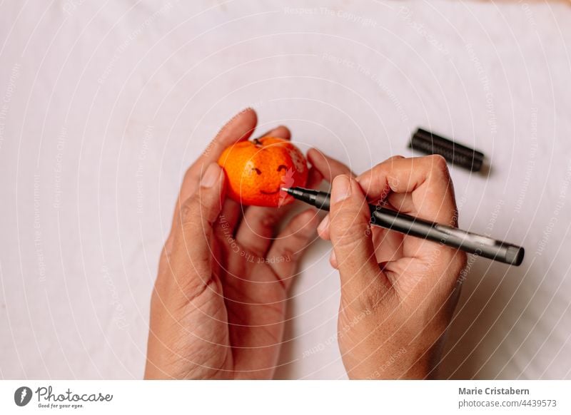 Top view of a woman drawing a smiley face on a clementine with her hands Clementine Oranges Smiley drawing top view Women's Hands Drawing mental health Wellness