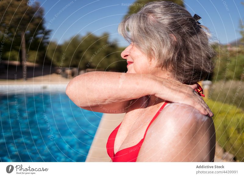 Smiling old woman smearing lotion while relaxing on poolside senior sunbath sunblock cream apply positive hydrate chill female carefree water gray hair summer