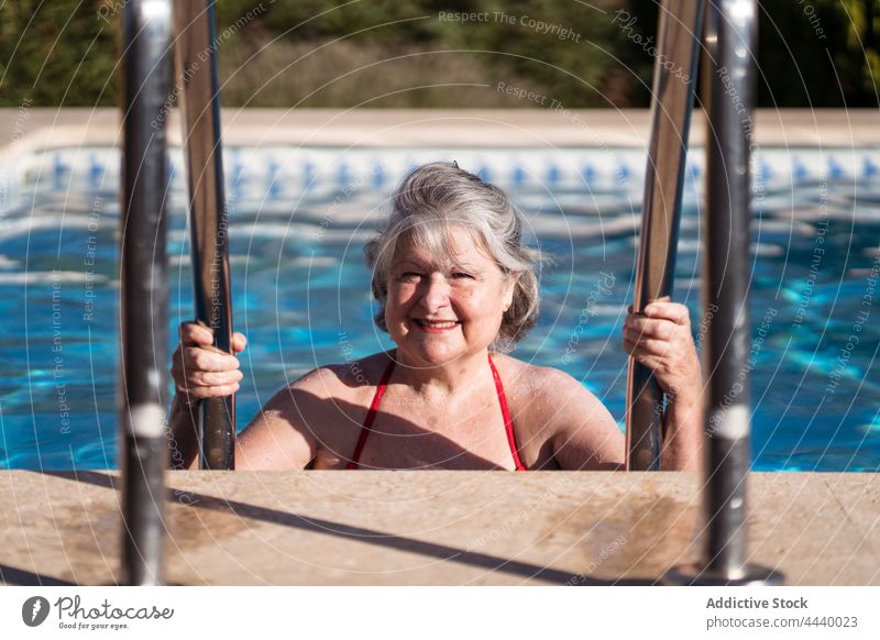Smiling old woman holding pool handrails while relaxing in water positive senior enjoy chill pleasure poolside female cheerful summer carefree travel gray hair