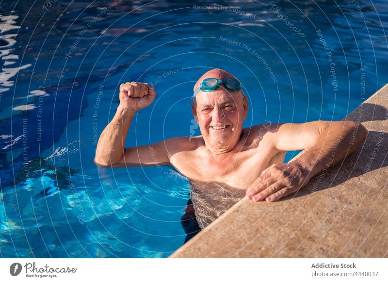 Old man raising fist up while swimming in pool senior power gesture blue water together show arms raised swimwear poolside glad wet symbol positive optimist