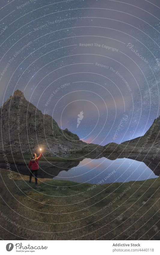 Anonymous traveler contemplating mountains and pond under Milky Way milky way nature highland landscape astronomy man night admire contemplate torch snowy