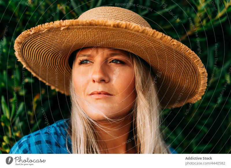 Dreamy traveler in straw hat against shrub wistful natural vacation reflective dreamy solitude woman portrait contemplative tourism garment trip